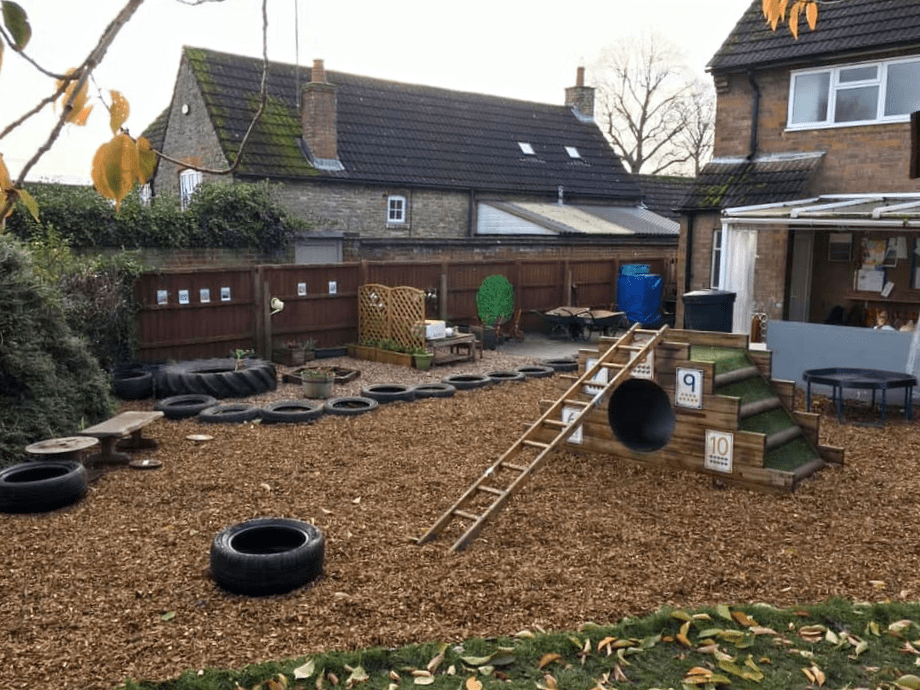 The preschool's outdoor area with bark chippings, tyres and a wooden climbing ramp