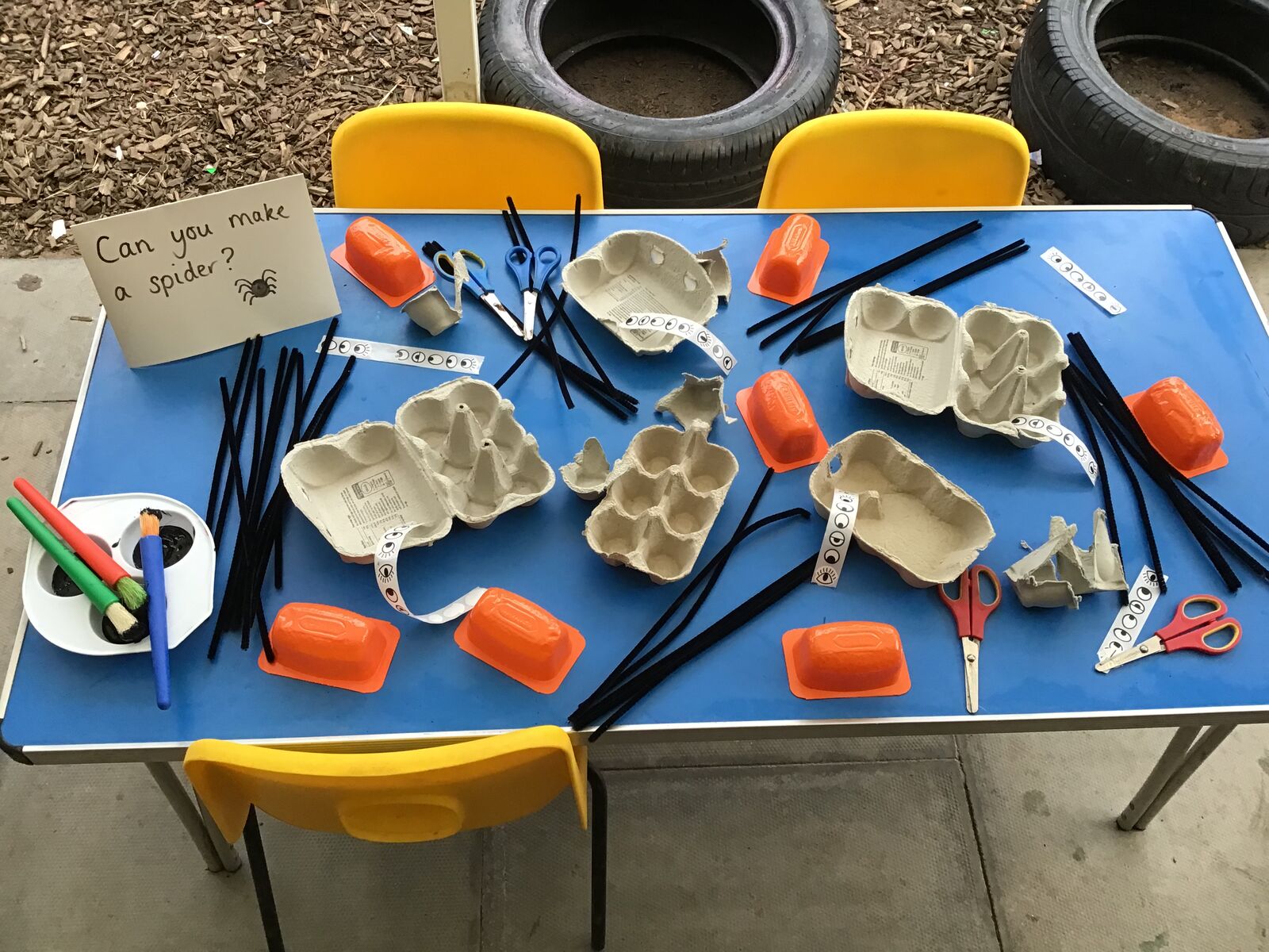 An outdoor table laid out with egg boxes, tongs and junk modelling materials