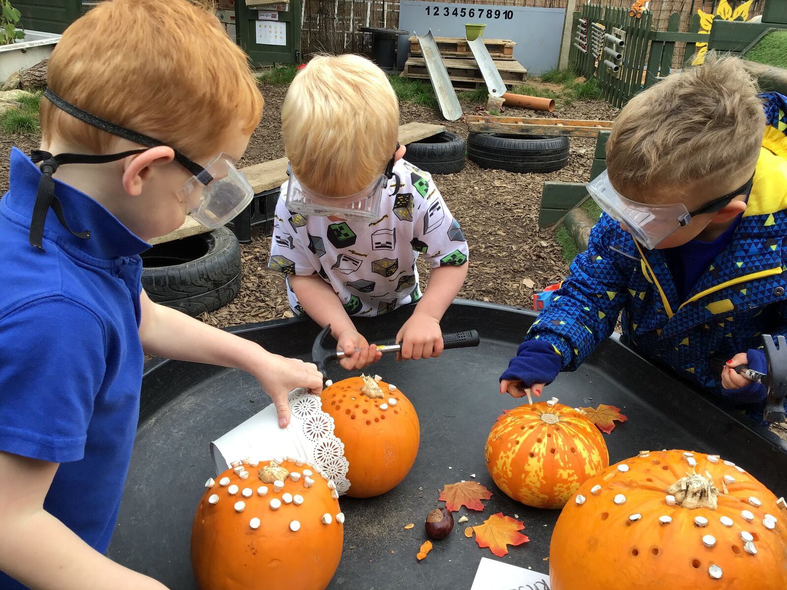 Three children in safety goggles decorating pumpkins together