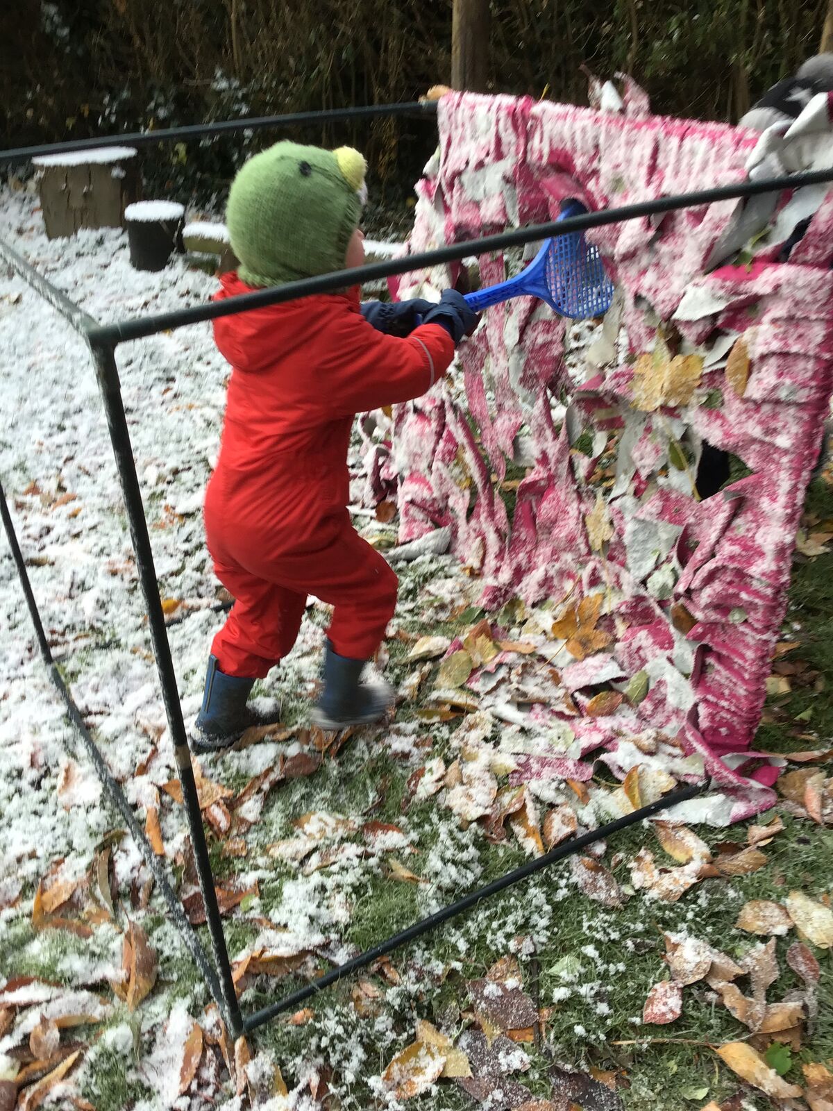 A child in a red all-in-one weaving fabric strips through an outdoor frame