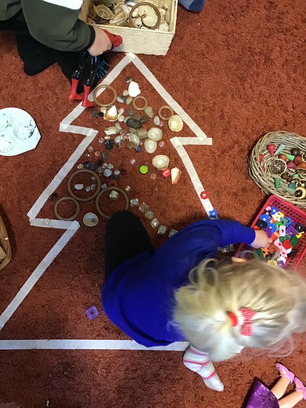 A child decorating a large Christmas tree outline marked out on the floor