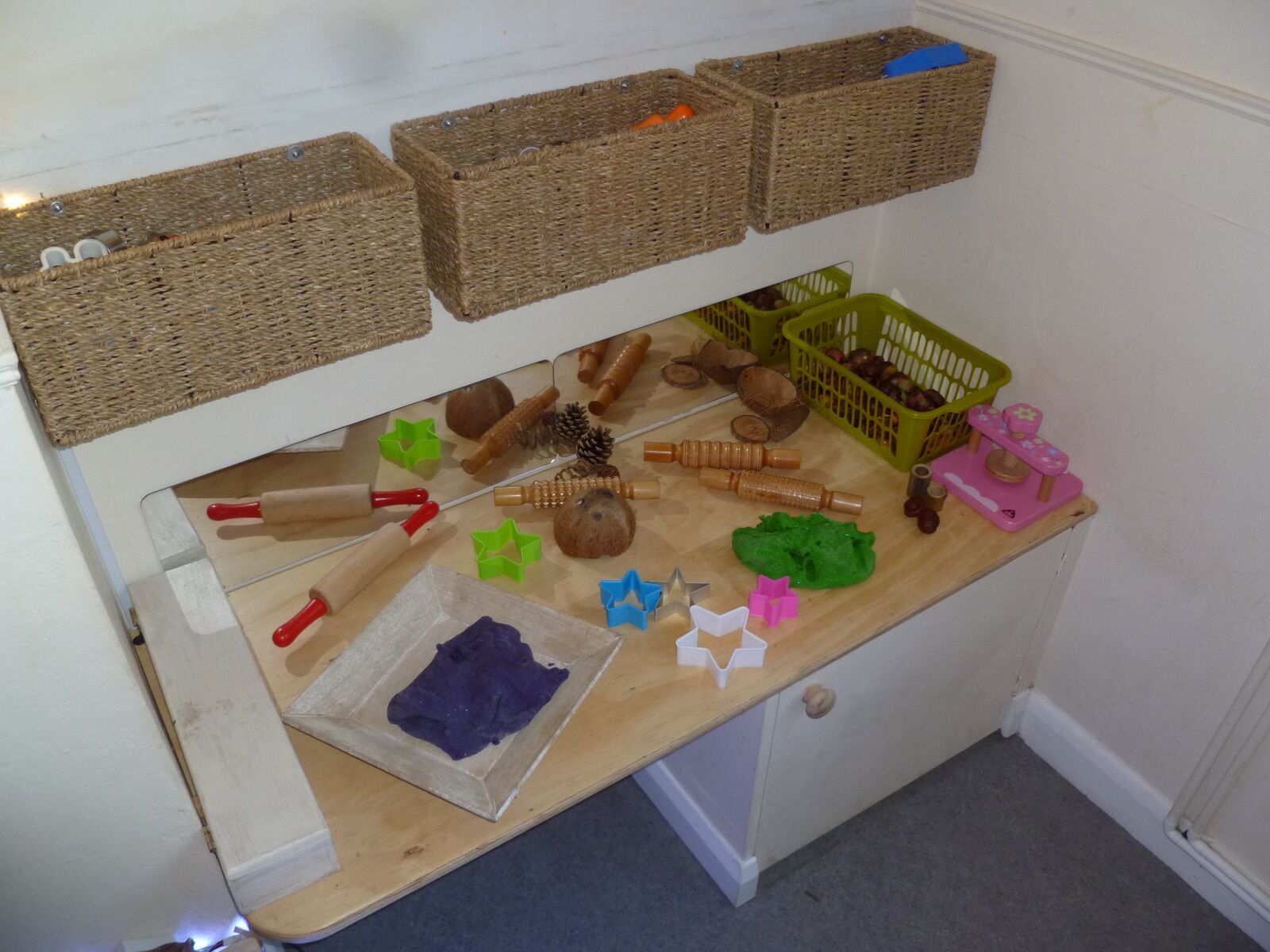 An indoor dough and loose parts table with wicker storage baskets above