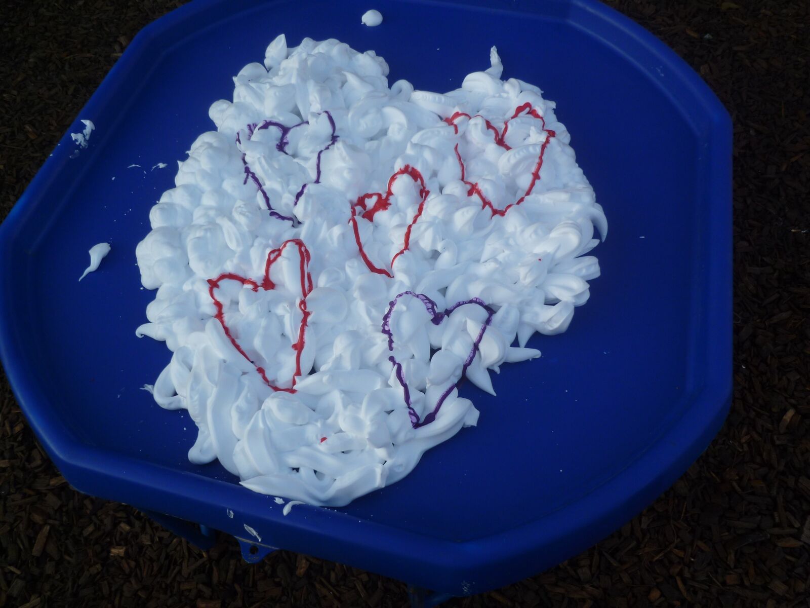 Hearts drawn into shaving foam spread across a blue tuff tray