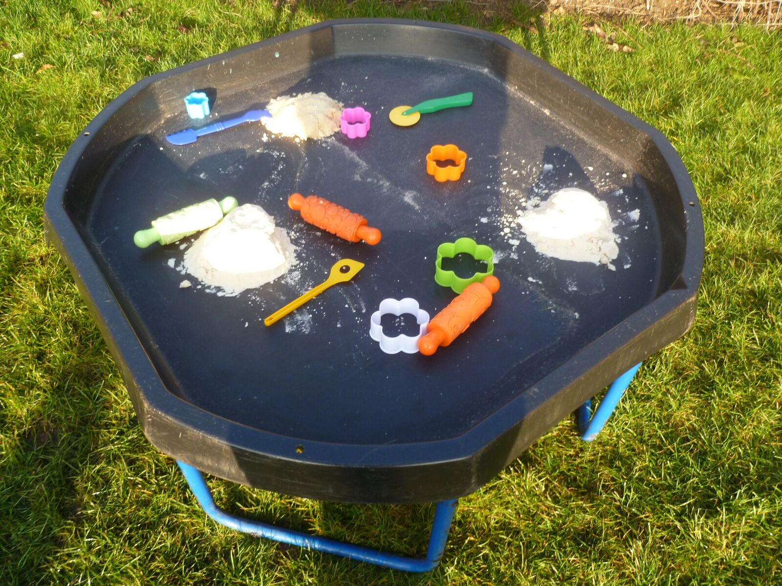A tuff tray of dough, cutters and play vegetables set up on the grass