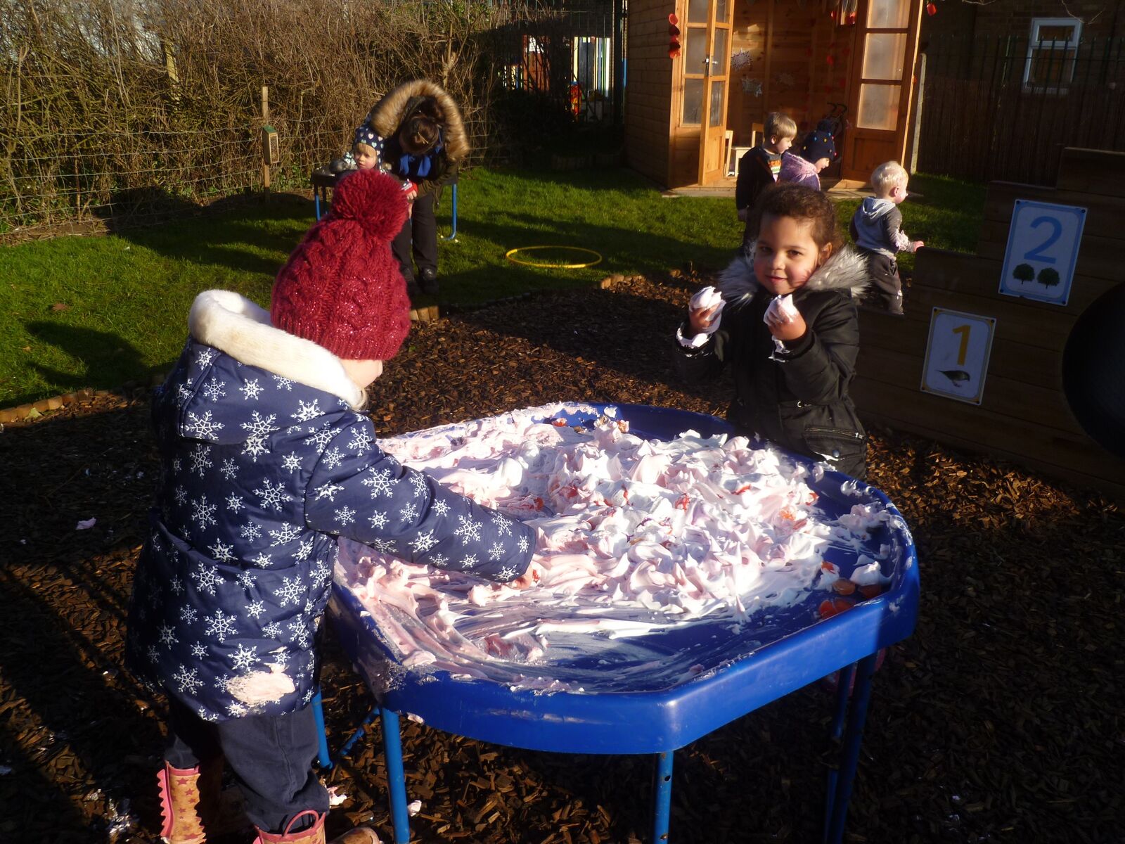 A child spreading shaving foam across a tray outdoors