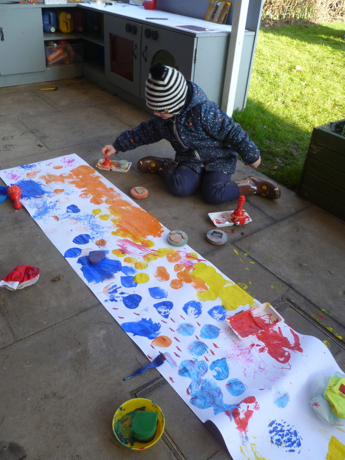 A child printing colours along a long roll of fabric outdoors