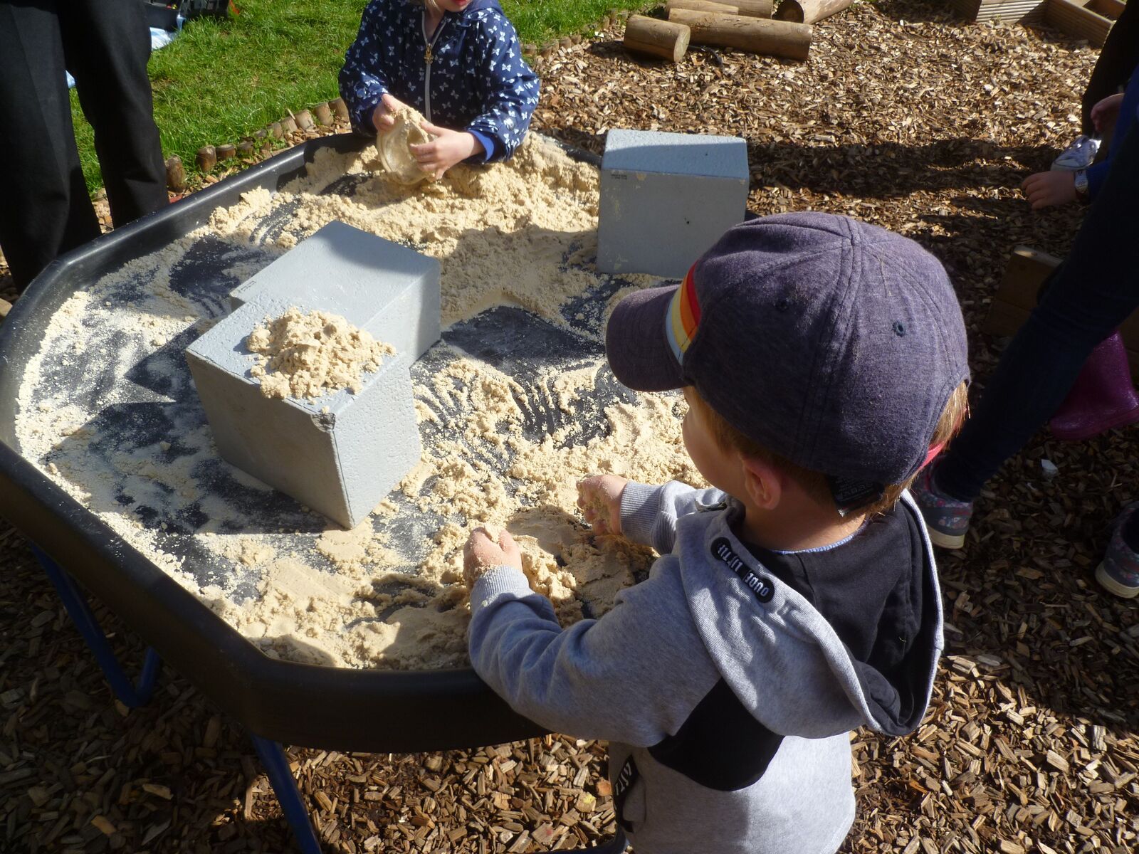 A child in a woolly hat building in the sand tray