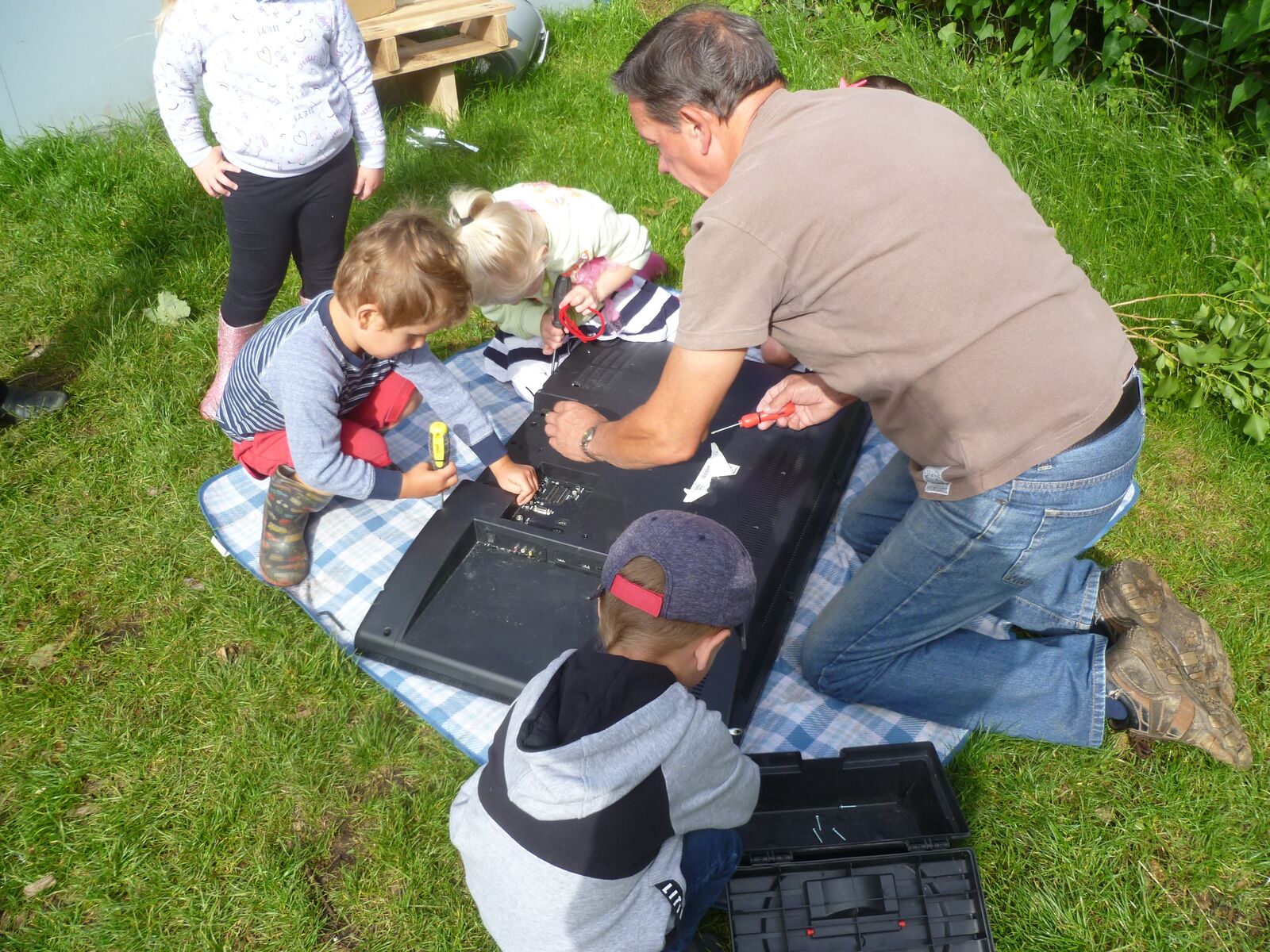 Children and an adult kneeling on the grass to plant seedlings