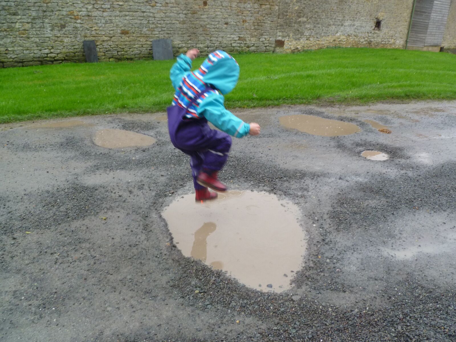 A child in waterproofs jumping into a puddle