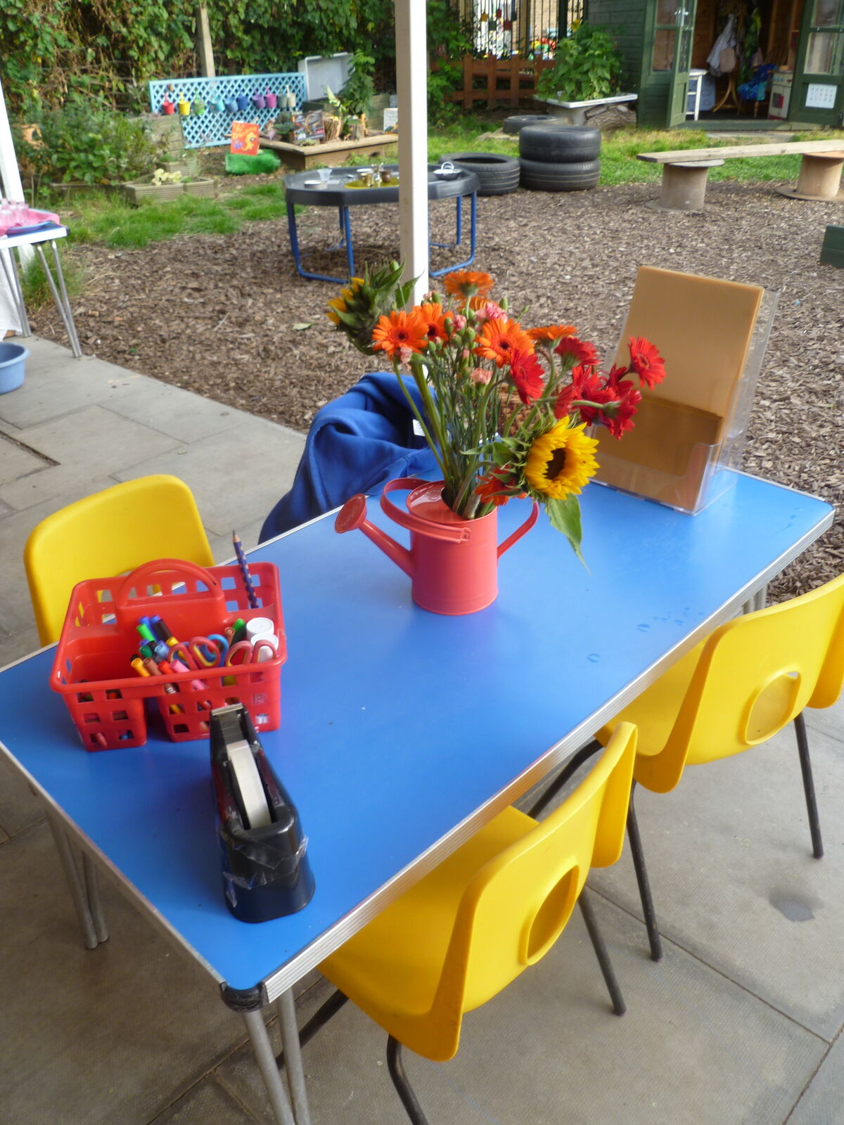 An outdoor table with jugs of sunflowers and a red watering can