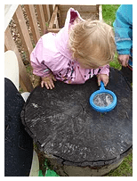 A child working at the tree stump table with a sieve